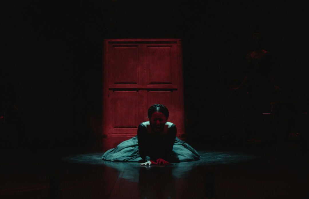 A performer on a dark stage in front of a red door